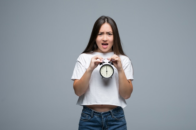 Sorriso asiático novo da mulher com um relógio isolado no fundo cinzento