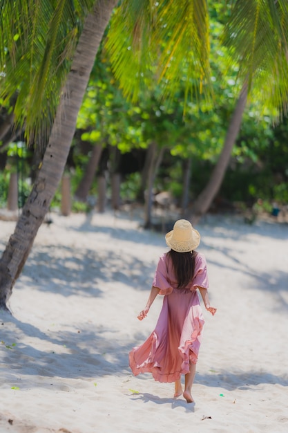 Sorriso asiático novo do retrato feliz em torno do oceano do mar da praia com a palmeira de coco para férias do feriado