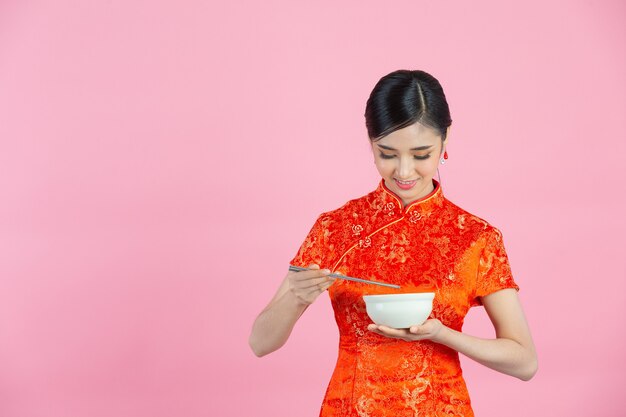 Sorriso feliz linda mulher asiática e comendo no ano novo chinês em fundo rosa.