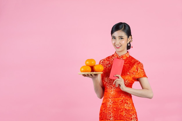 Sorriso feliz linda mulher asiática e segurando laranjas frescas no ano novo chinês em fundo rosa.