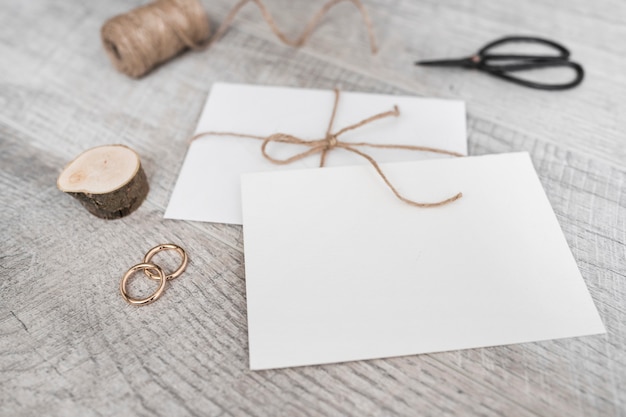 Foto grátis spool; toco de árvore em miniatura; alianças de casamento; tesoura e envelope branco sobre fundo de madeira