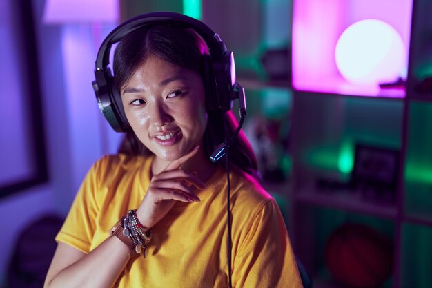 Streamer de mulher chinesa sorrindo confiante usando fone de ouvido na sala de jogos