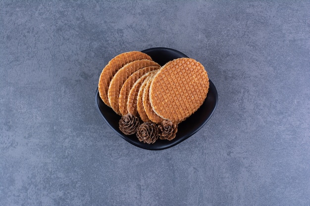 Stroopwafels com pinhas isoladas em uma placa preta sobre uma pedra.