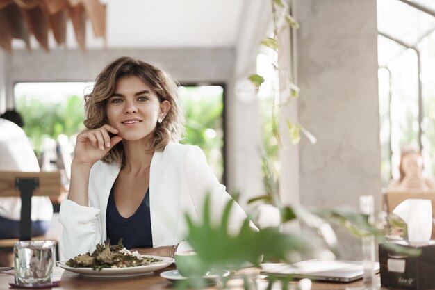 Stylush sucesso ambicioso atraente jovem especialista em marketing feminino sentar restaurante café moderno comer salada saudável beber café sorrindo deliciado encontro de negócios durante o almoço, discutir o trabalho.