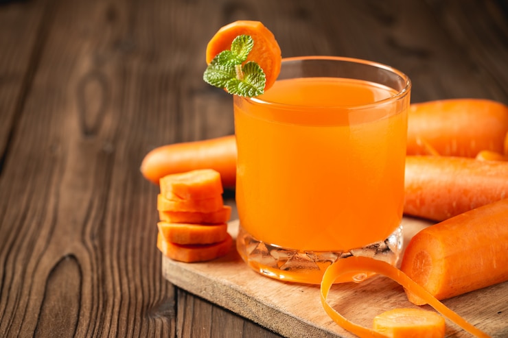 Foto grátis suco de cenoura em vidro na mesa de madeira.