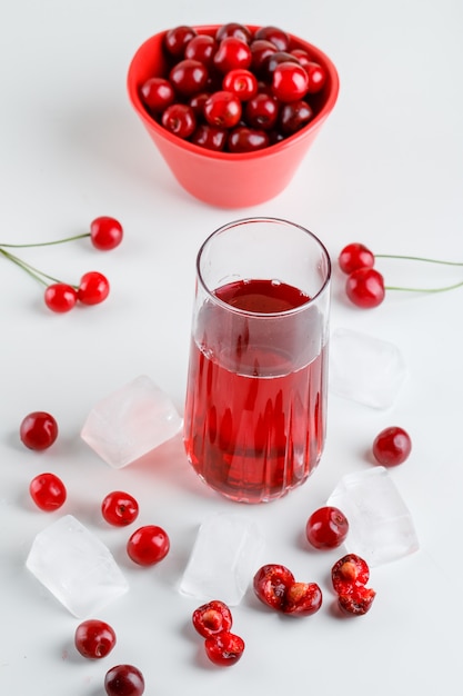 Suco de cereja com cerejas, cubos de gelo em um copo em branco