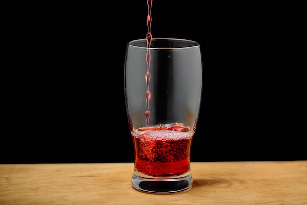 Suco de cereja derramando em vidro na mesa de madeira