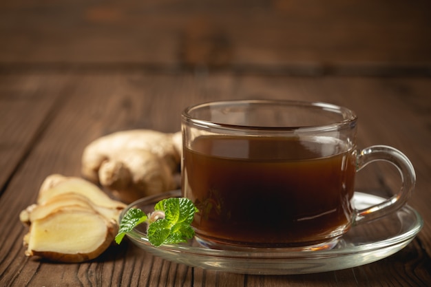 Suco de gengibre quente e gengibre fatiado na mesa de madeira.