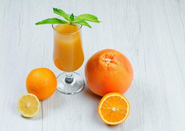 Suco de laranja com hortelã, laranja, limão, toranja em um cálice na superfície de madeira branca, vista de alto ângulo.