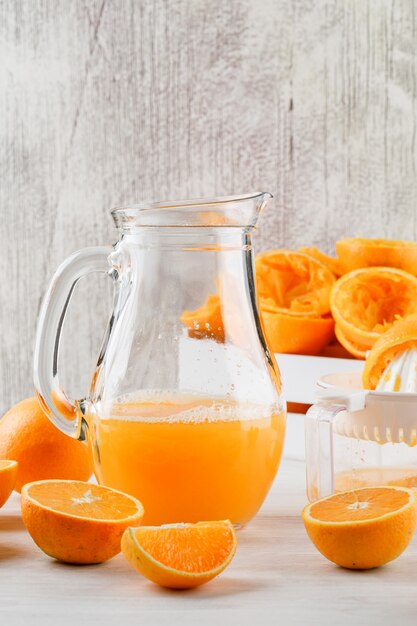 Suco de laranja com laranjas, espremedor de frutas em uma jarra na superfície branca