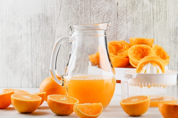 Suco de laranja com laranjas, espremedor de frutas em uma jarra na superfície branca