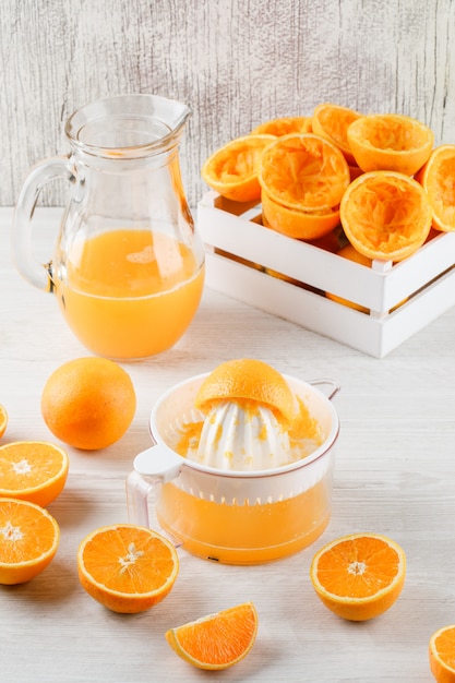 Suco de laranja em uma jarra com laranjas, espremedor vista de alto ângulo na superfície de madeira