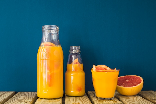 Foto grátis suco de toranja na garrafa e copo na mesa de madeira contra o pano de fundo azul