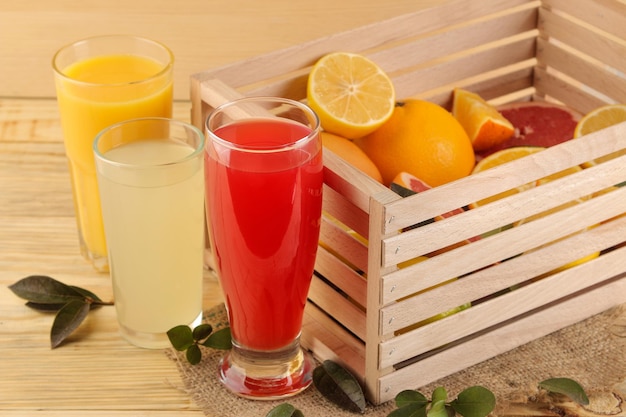 Sucos cítricos. suco de laranja, limão e toranja com frutas frescas em uma caixa sobre fundo de madeira natural