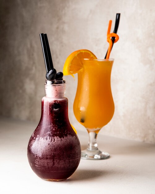 Sucos de laranja e uva com frutas dentro do copo e da jarra.