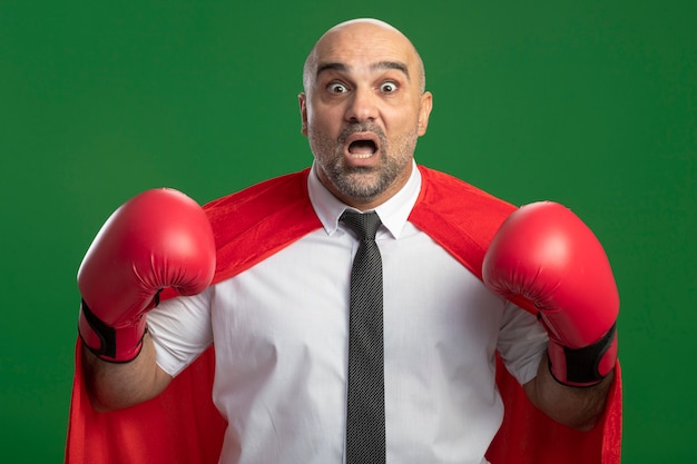 Foto grátis super-herói empresário com capa vermelha e luvas de boxe erguendo as mãos, olhando para a frente, assustado, gritando em pé sobre a parede de luz