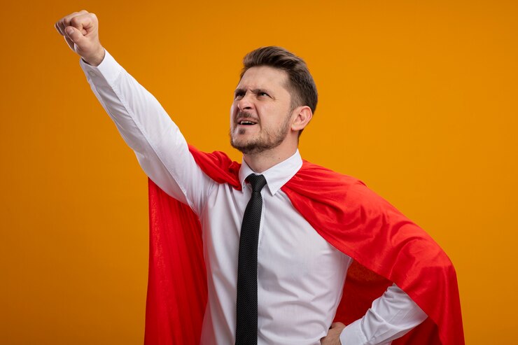 Foto grátis super-herói empresário com capa vermelha olhando para cima, fazendo um gesto vencedor pronto para ajudar em pé sobre um fundo laranja