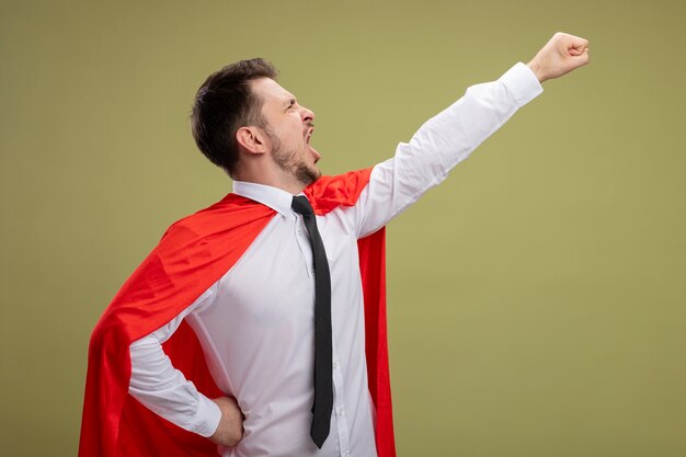 Foto grátis super-herói empresário com capa vermelha segurando o braço em gesto voador e gritando pronto para lutar em pé sobre fundo verde