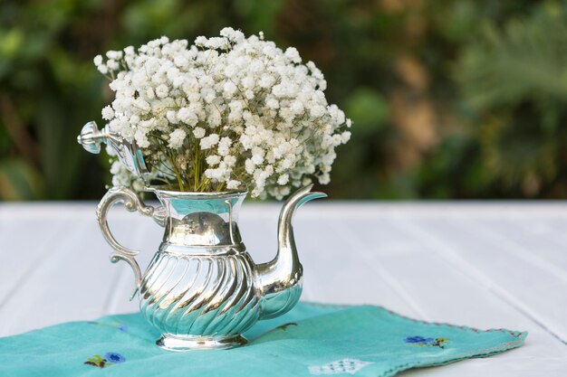 Superfície com toalha de mesa e bule cheio de flores