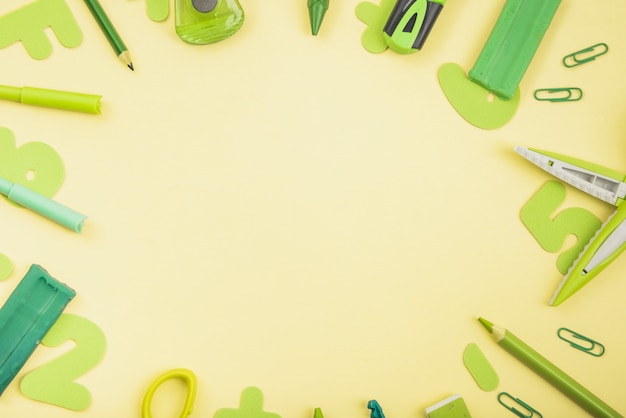 Foto grátis suprimentos escolares de cor verde dispostos em forma circular sobre fundo amarelo