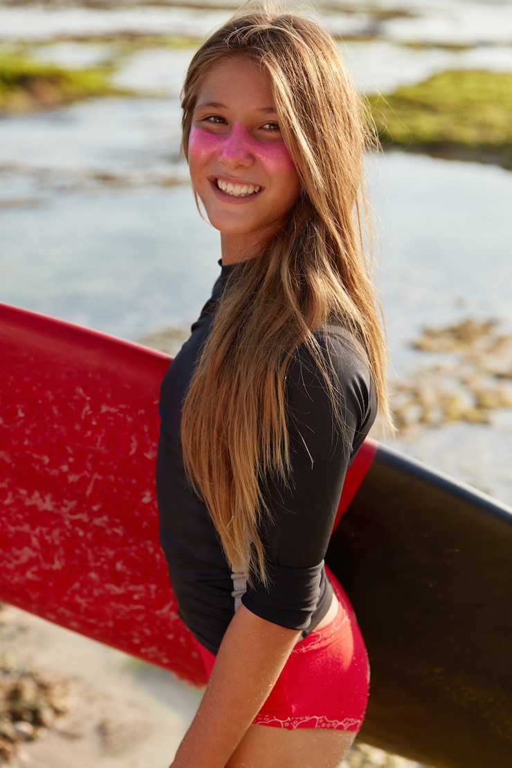 Foto grátis surfista ativo sorridente tem expressão satisfeita, cabelo comprido, protetor solar protetor no rosto