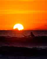 Foto grátis surfista sentado no oceano ao pôr do sol