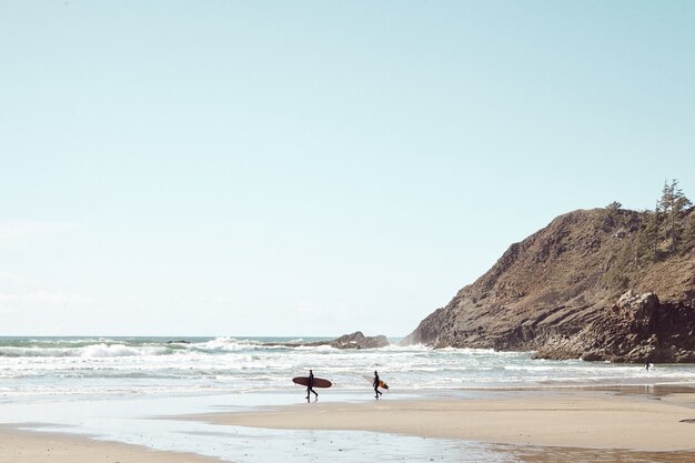 Surfistas à distância em praia rochosa