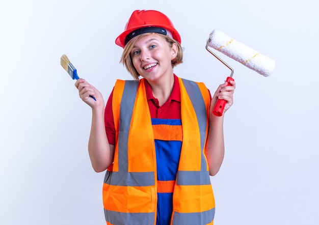 Foto grátis surpreendeu a jovem construtora de uniforme segurando uma escova giratória com pincel isolado na parede branca
