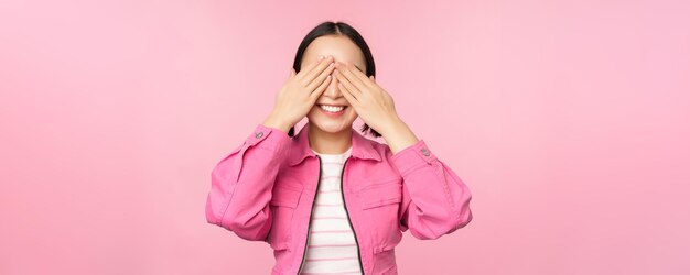 Surpresa e celebração Retrato de menina feliz asiática fecha os olhos esperando o presente antecipando algo de pé surpreendido contra o fundo do estúdio Copiar espaço