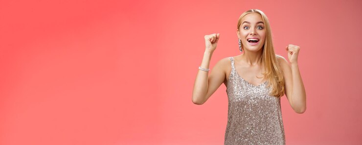 Foto grátis surpresa feliz celebrando uma jovem loira com um vestido prateado da moda levantando as mãos sim vitória ge