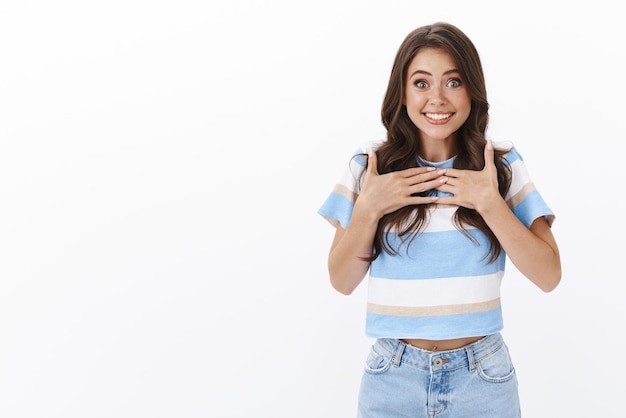 Foto grátis surpresa, sortuda, fofa, otimista, parece esperançosa, desejando ser escolhida, toque no peito apontando-se sorrindo, feliz por receber um prêmio incrível em pé, fundo branco, aprecie um presente incrível