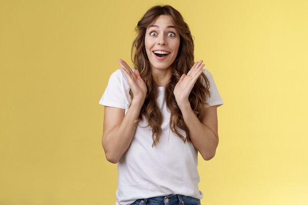 Surpreso feliz satisfeito impressionado menina de cabelos cacheados olhar câmera admiração satisfação alegria aplauso palmas alegre sorrindo amplamente olhar câmera fascinado aplauso entusiasmado fundo amarelo