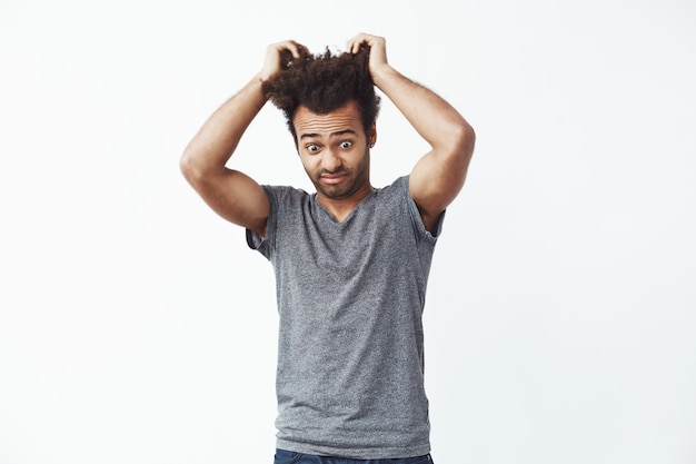 Surpreso homem africano descontente, olhando para baixo, tocar no cabelo.