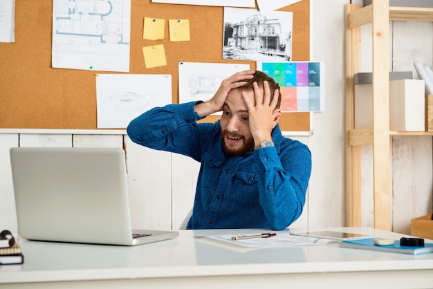 Surpreso jovem empresário de sucesso sorrindo, sentado no local de trabalho com computador portátil