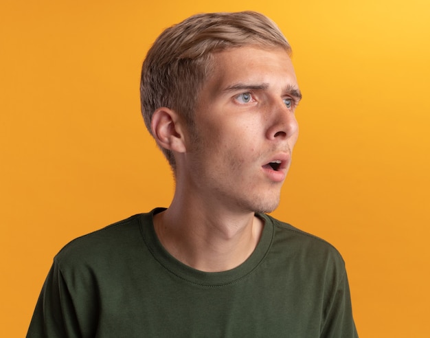 Foto grátis surpreso olhando para o lado jovem bonito vestindo camisa verde isolada na parede amarela