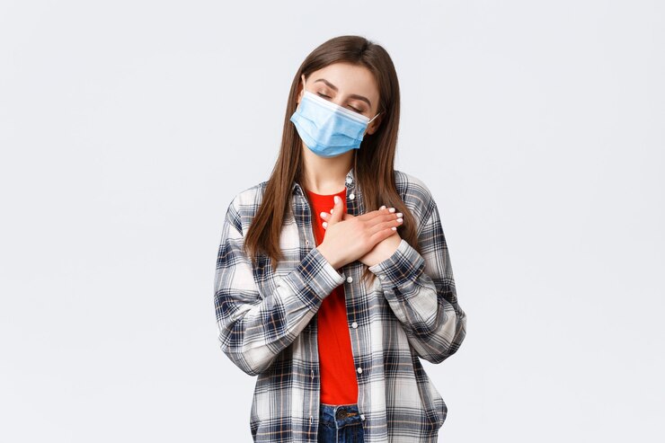 Foto grátis surto de coronavírus, lazer na quarentena, distanciamento social e conceito de emoções. mulher jovem e atraente sonhadora em máscara médica, feche os olhos de imagem ou lembre-se da memória, pressione as mãos no coração