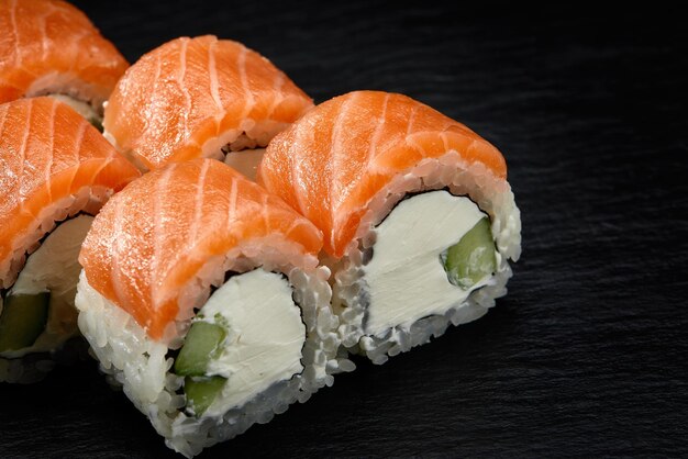 Sushi de rolo filadélfia com pepino de salmão e queijo creme em fundo preto para menu de comida japonesa
