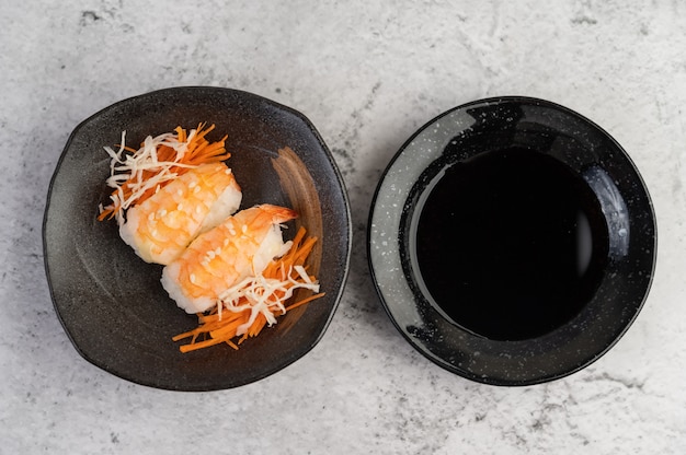 Sushi é um prato com molho sobre um piso de cimento branco.