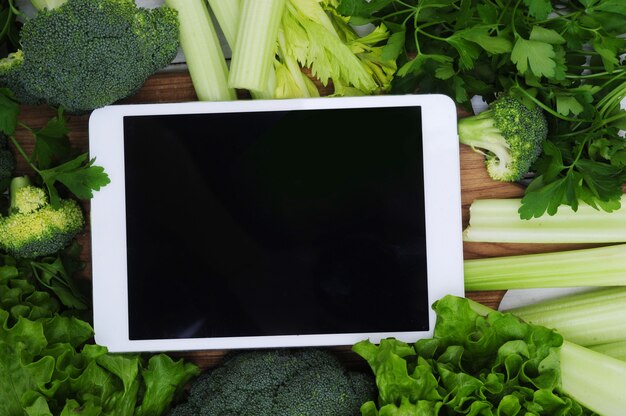 Tablet digital com tela em branco, cercada por legumes, conceito de comida saudável