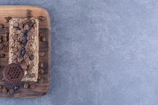 Tábua de madeira sob uma fatia de bolo com biscoito e grãos de café na superfície de mármore