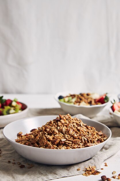 Taças de granola com iogurte, frutas e morangos em uma superfície branca