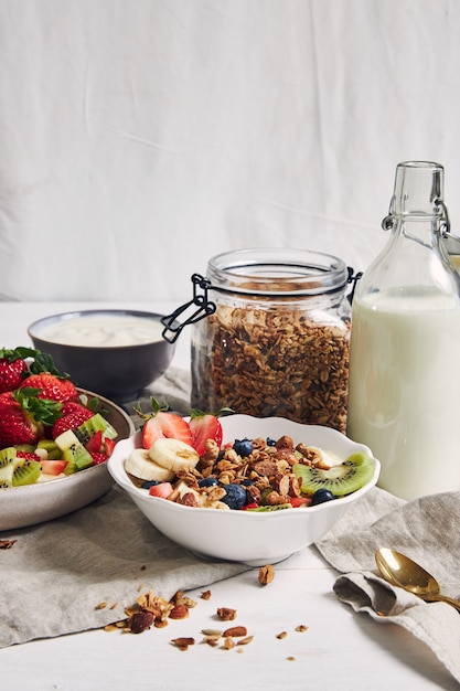 Taças de granola com iogurte, frutas e morangos em uma superfície branca