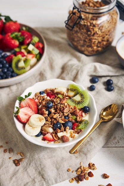 Taças de granola com iogurte, frutas e morangos em uma superfície branca