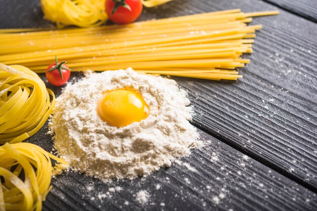 Tagliatelle e espaguete com gema de ovo na farinha sobre a mesa de madeira