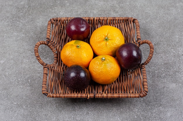 Tangerinas doces frescas com ameixas em uma cesta de vime