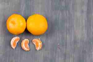 Foto grátis tangerinas frescas e segmentos na mesa de madeira