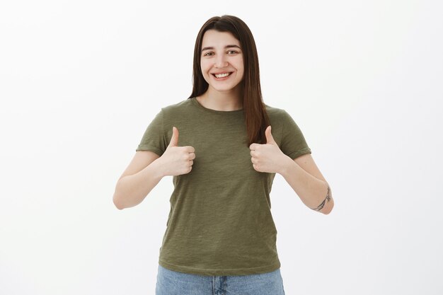 Tão incrível, como sua ideia. Retrato de alegre e satisfeita linda garota dos anos 20 com tatuagem sorrindo encantada e alegre mostrando os polegares para cima em gesto de aprovação e apoio, reagindo à excelente sugestão