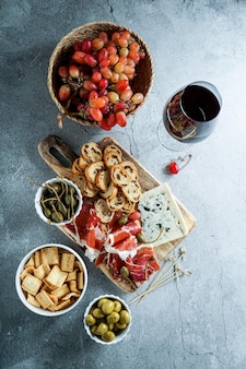 Tapas tradicionais espanholas ou italianas. jamon ibérico, queijo azul, bolachas, azeitonas, uvas e vinho tinto seco, fundo de pedra cinzenta. vista do topo