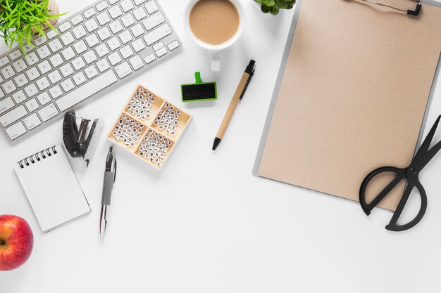 Teclado com material de escritório; chá e maçã no fundo branco