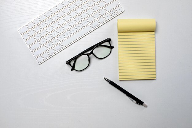 Teclado sem fio e bloco de notas amarelo com óculos em cima da mesa